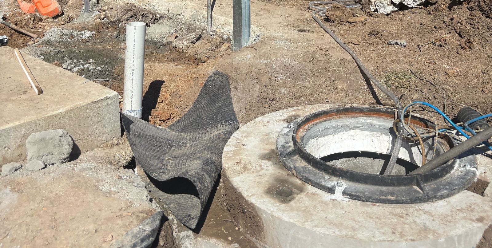 New concrete manhole installed at a residential site, with surrounding excavation and services